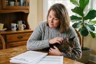 Femme tenant son chat tigré sur ses genoux tout en consultant des documents de mutuelle animale sur une table en bois